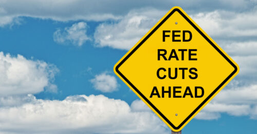 Yellow caution road sign against cloudy blue sky with text FED RATE CUTS AHEAD